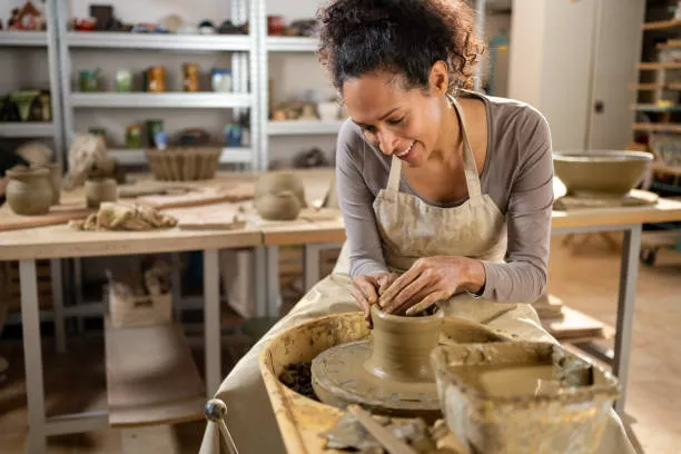 Professional portrait of Sophie Leclair in contemporary studio space with modern sculptural works, smiling while working with ceramic materials
